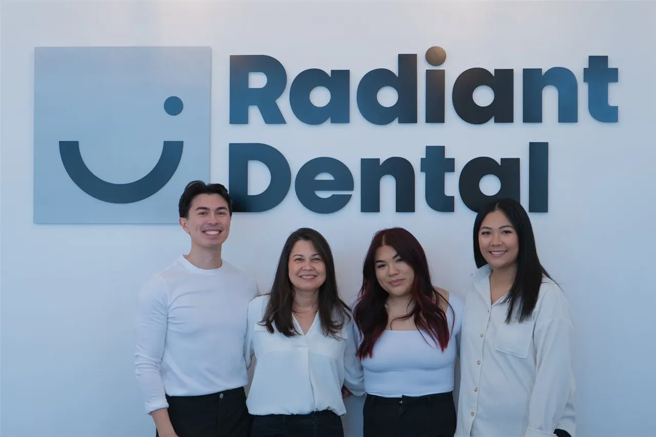 The Radiant Dental team standing in front of the clinic logo wall